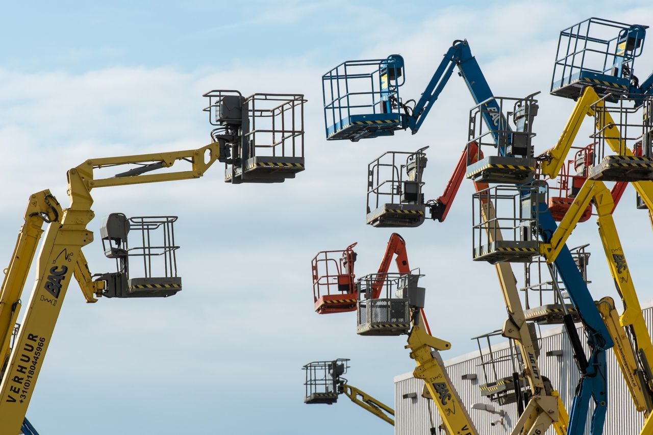 story-02 A collection of colorful boom lifts reaching toward a clear blue sky, showcasing industrial machinery.