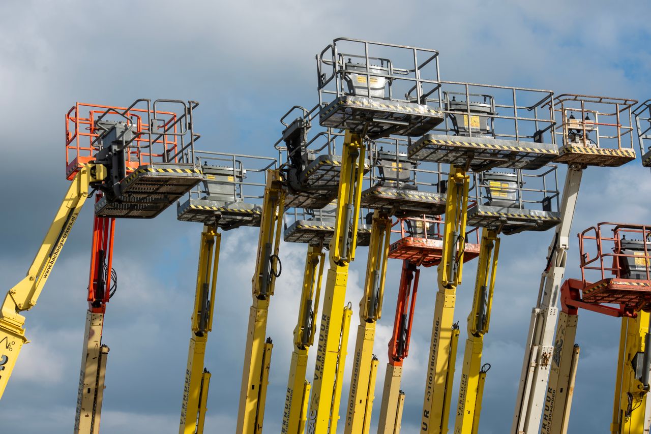 services-03 Multiple aerial work platforms with colorful booms reaching skyward against a cloud-dotted backdrop.
